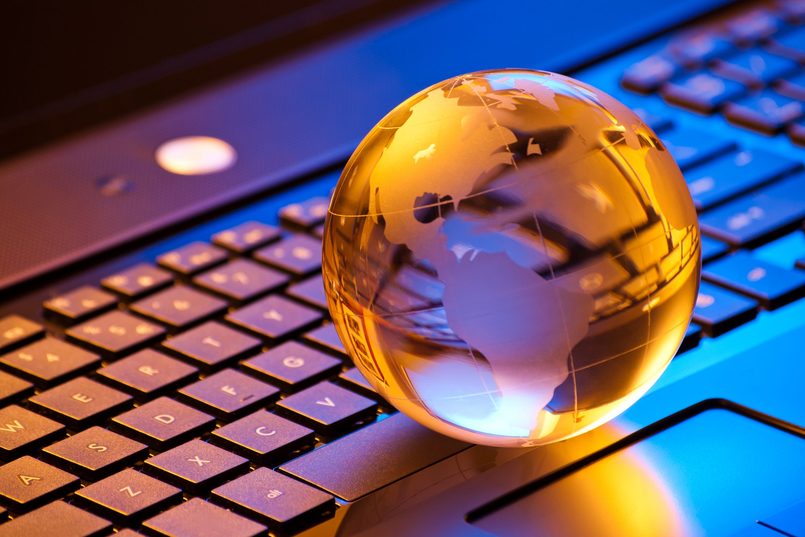global computer business concept with small globe on laptop keyboard in mixed light